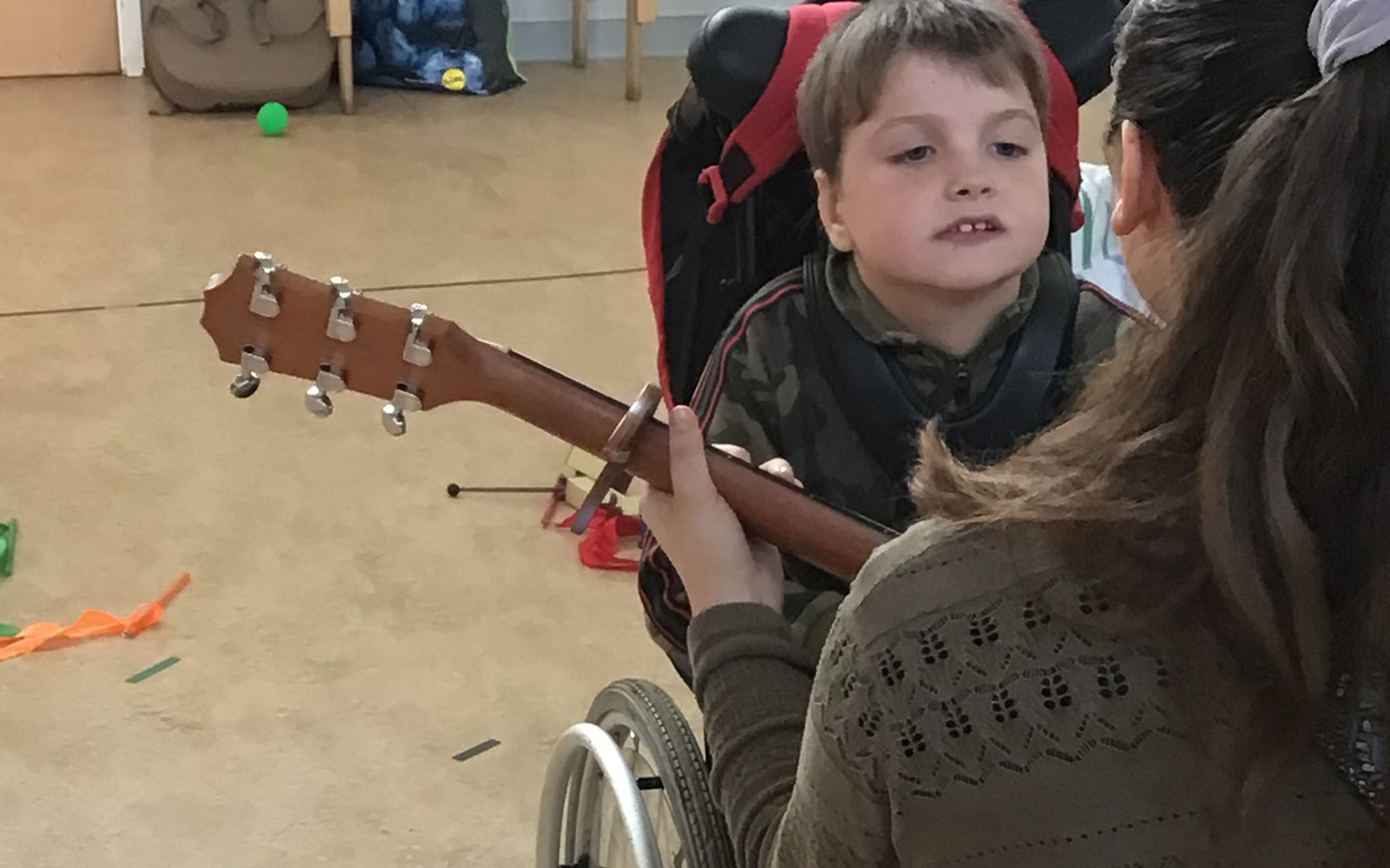 A young boy in a wheelchair listens and watches as a musician plays a guitar