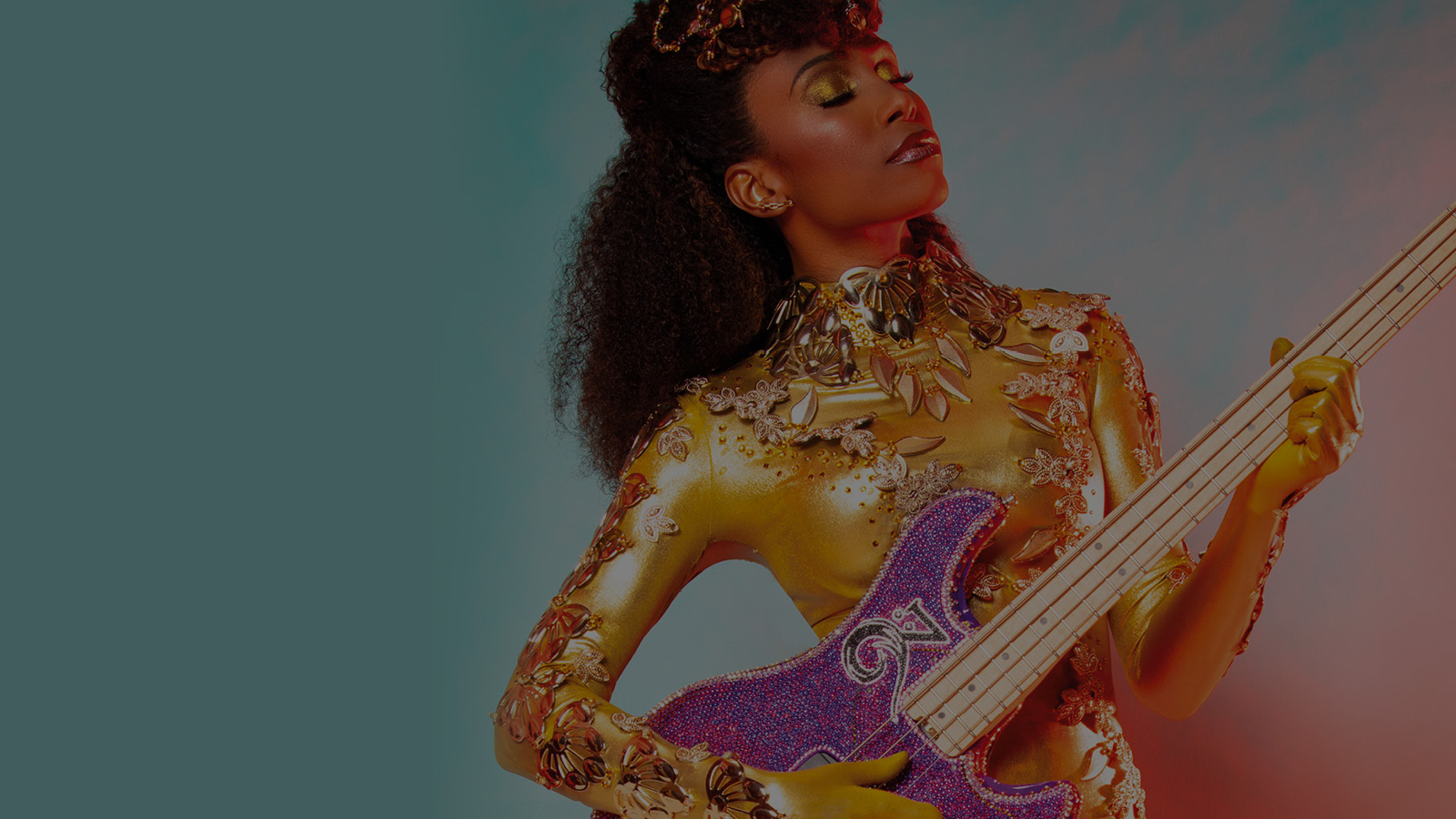 Bassist and vocalist Nik West wearing a glorious bejewelled gold headpiece and outfit playing the electric bass.