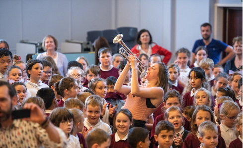 A woman plays trumpet in a crowd of children