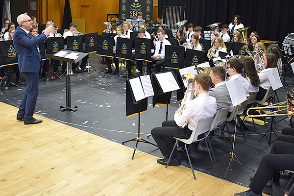 The National Youth Brass Band of Scotland during a performance conducted by Ian Porthouse. Young musicians sit in orchestral formation as Ian directs their performance.