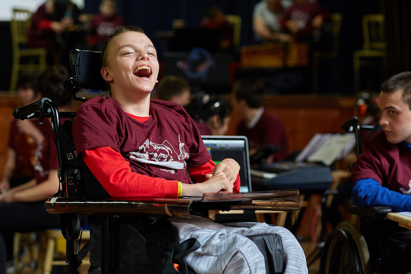 A child in a wheelchair smiles in a room full of people
