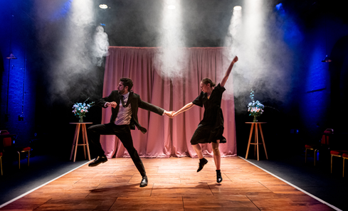 Two dancers look exuberant on stage in outfits you might wear to a funeral - black formalwear