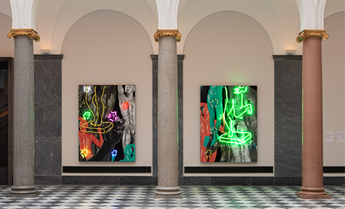 An art gallery. Two large brightly coloured and brightly lit artwork sit inside the recesses of two tall white arches. The floor is black and white and tall pillar rise up to support the high ceilings.  
