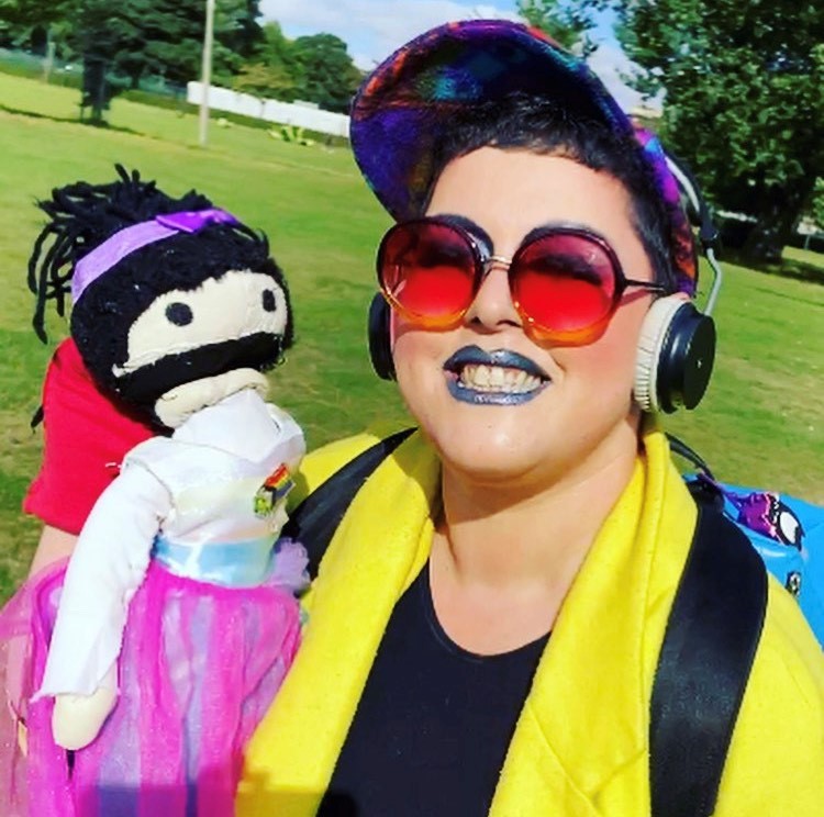 Miss Annabel Sings stands in a park with a puppet wearing bright sunglasses