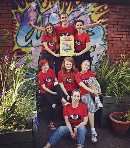 A group of volunteers stand in front of a graffiti wall in red tshirts