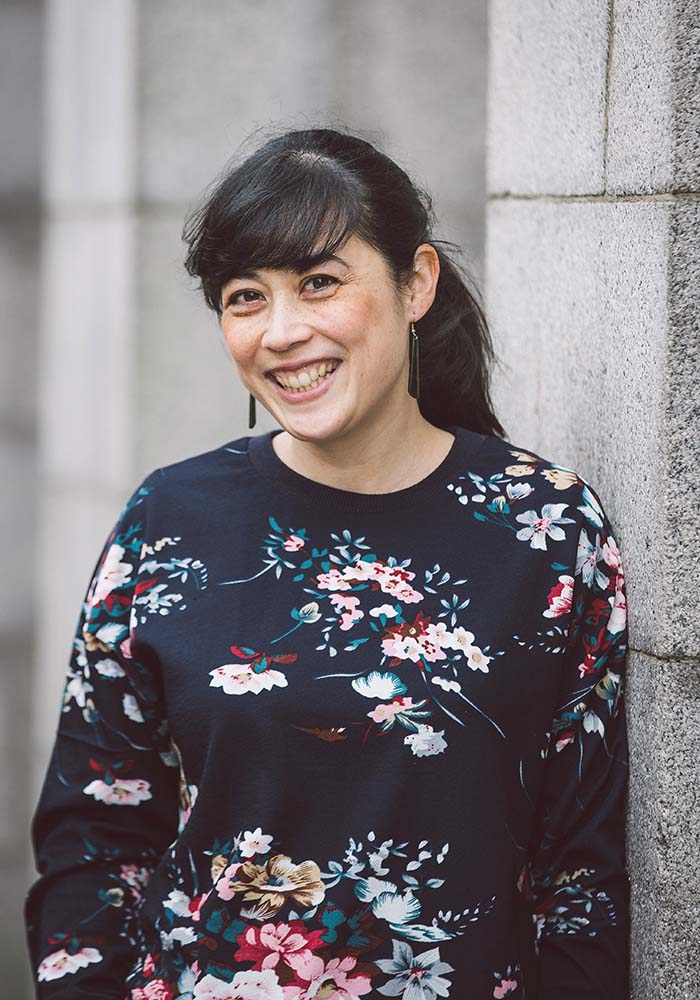 A person wearing a floral patterned long-sleeve shirt stands against a stone wall, blending style with a natural outdoor setting.