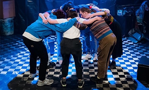 A group of performers stand in a huddle on the stage