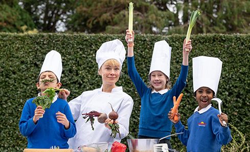 A group of children stand with a woman all wearing chefs hats