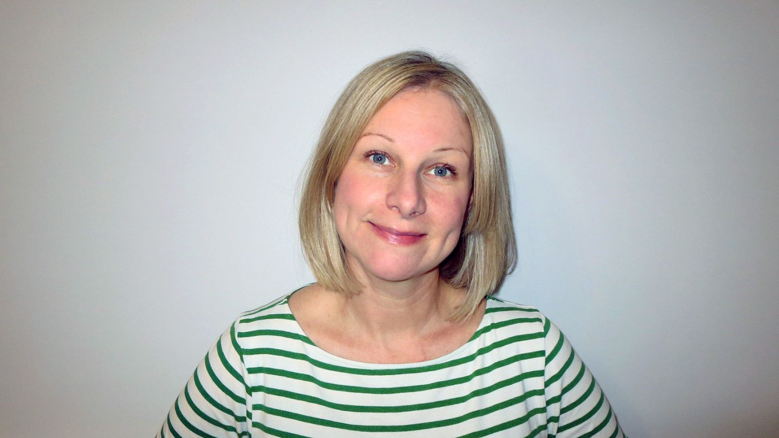A white woman with shoulder-length blonde hair is wearing a green and white striped shirt, against a light gray background. This is Jen Hunter.