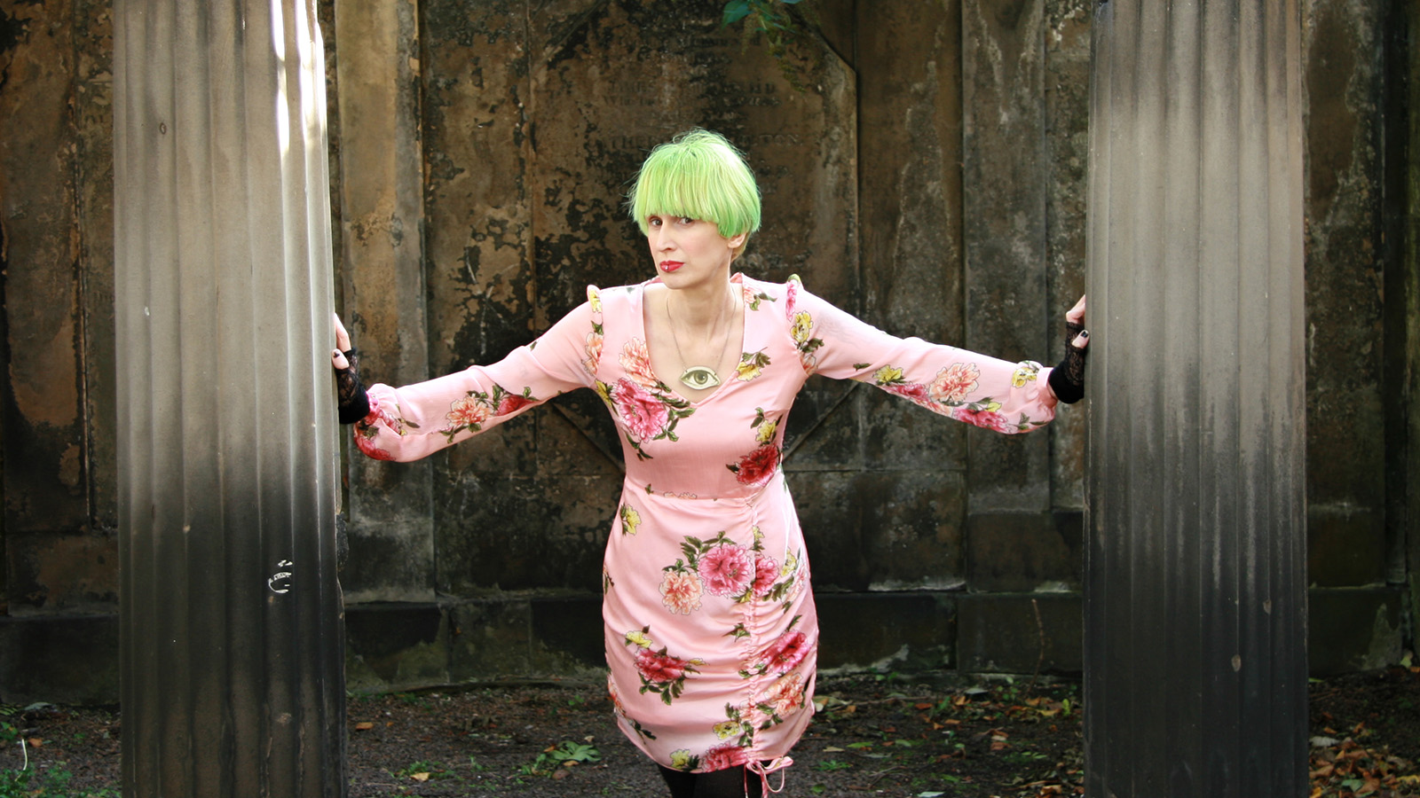 The author Ever Dundas is a woman with green hair wearing a boldly printed pink dress
