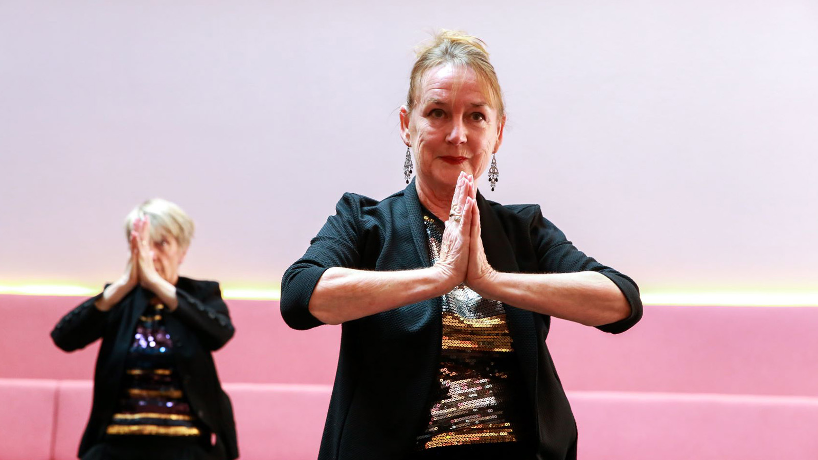 Two women stand with their hands in a prayer position