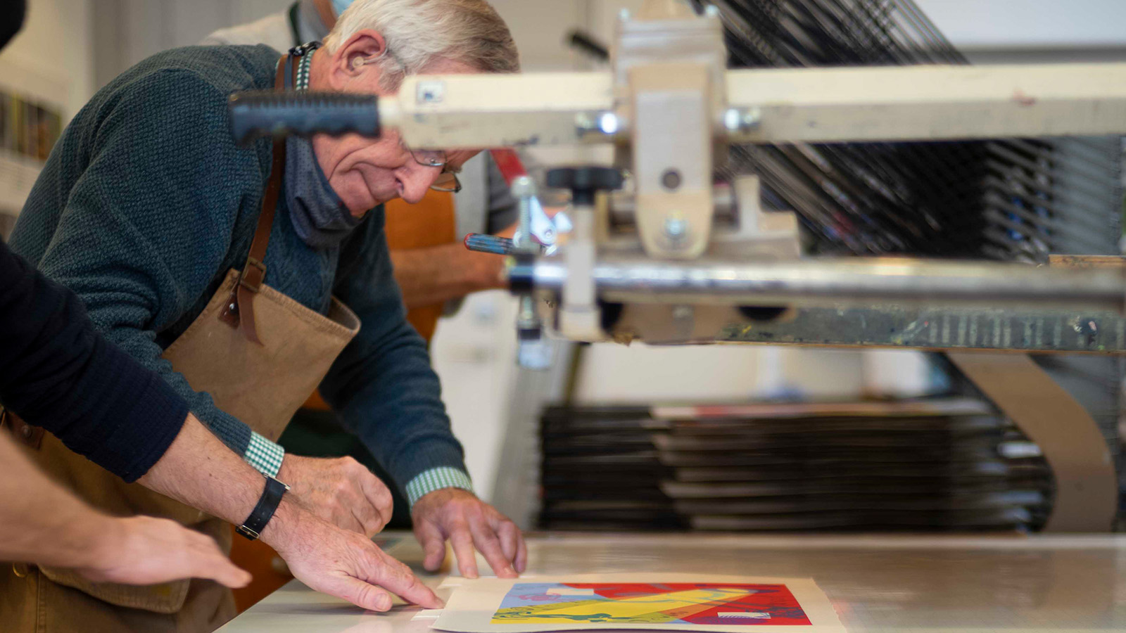 A group of older men work together on a colourful print at a print studio