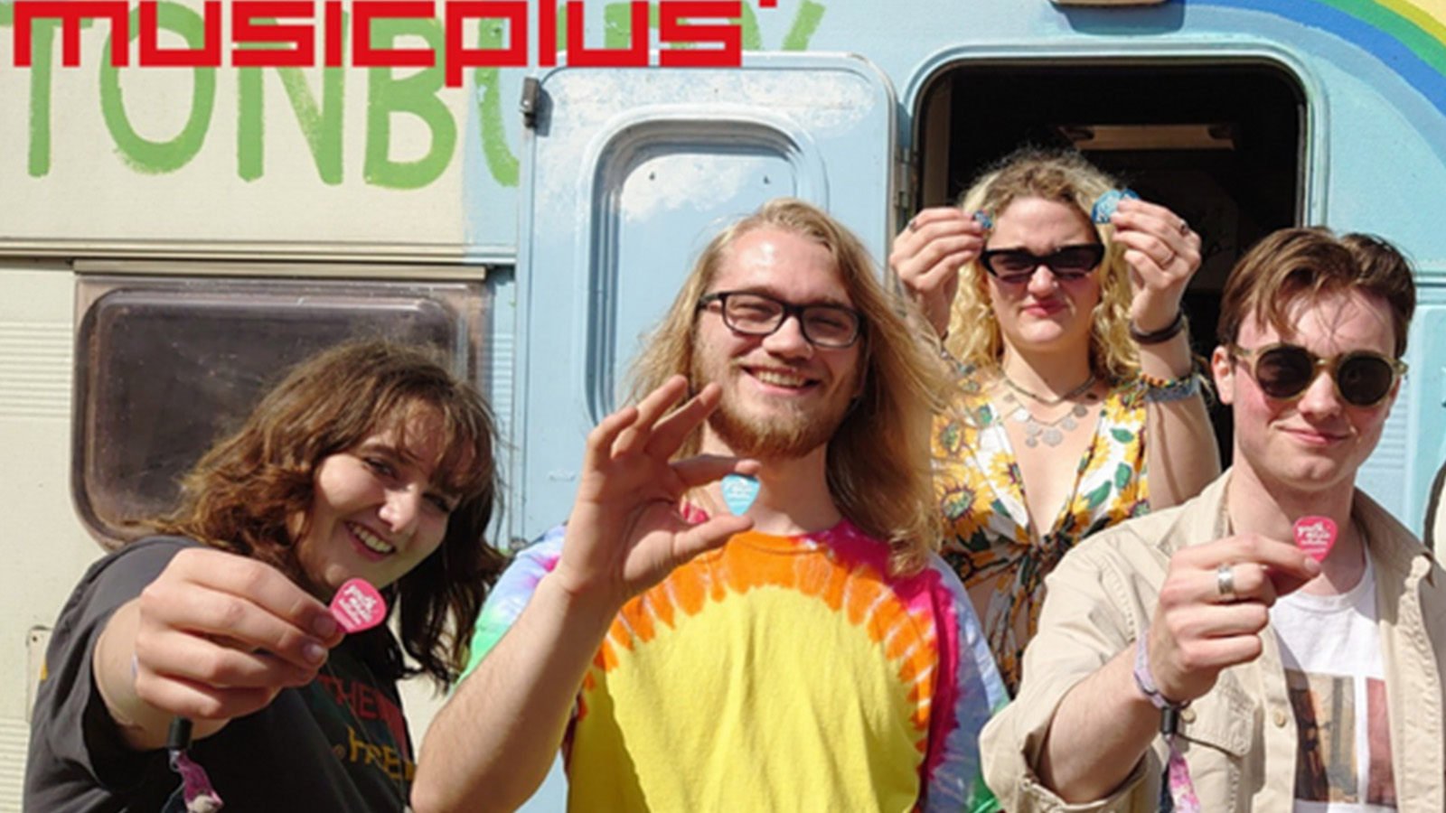 A group of young people smile together as they hold out YMI 20th anniversary pins, standing in front of a colourful background