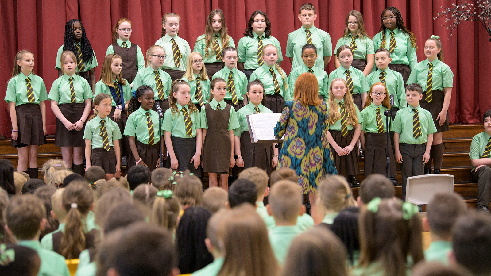 Boys and girls perform in a choir at their school before an audience of their friends and pupils