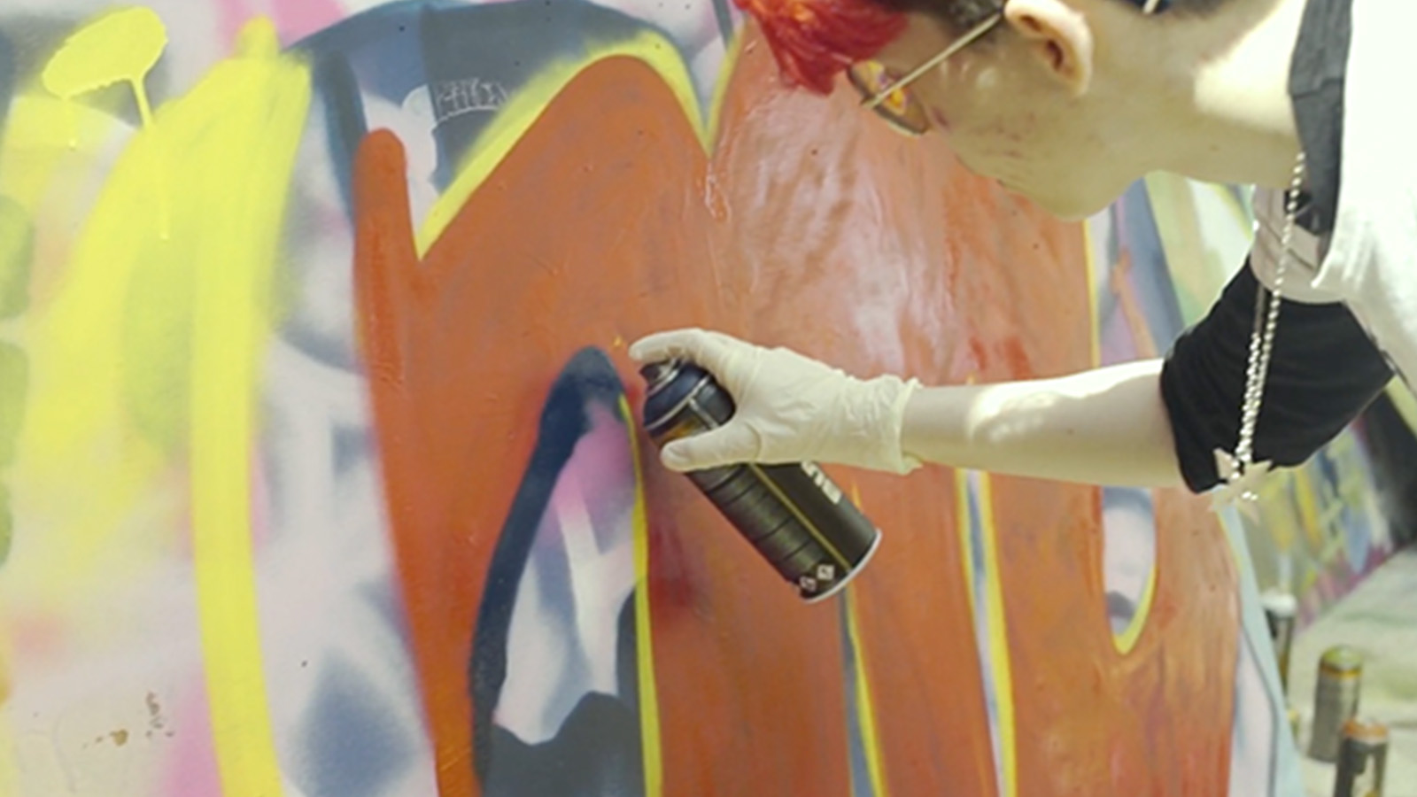 A young person carefully examines their artwork as they apply spraypaint