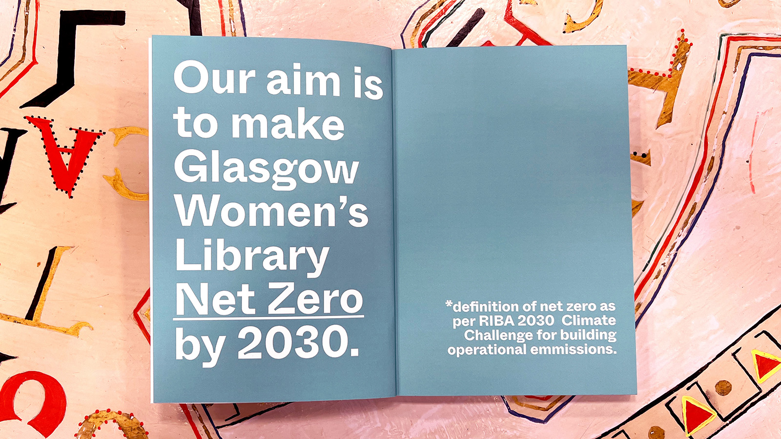 A book lies open, prominently displaying the words "Our aim is to make Glasgow Women's Library net-zero by 2030"