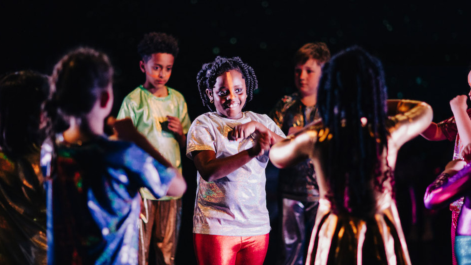 Young children in brightly coloured costumes perform on stage together