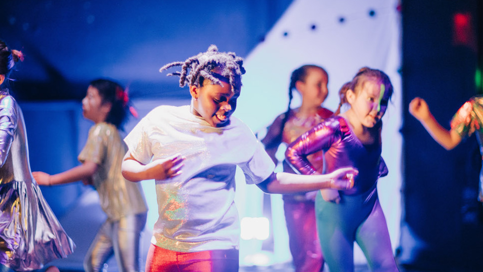 Young children in brightly coloured costumes perform on stage together