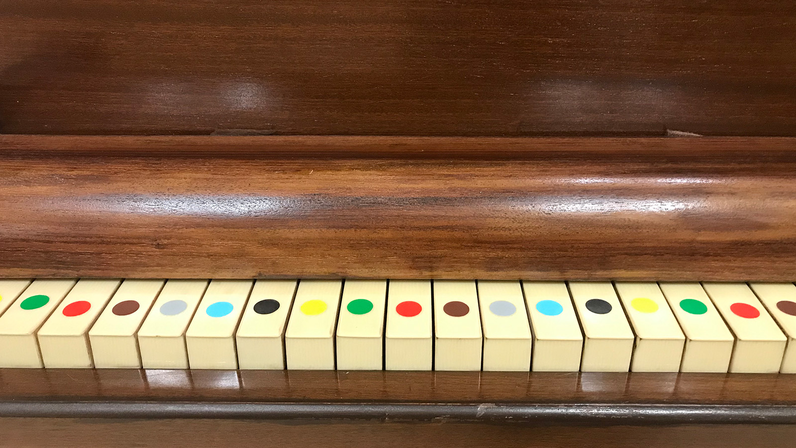 A piano with colourful round stickers on the keys indicating which notes are which