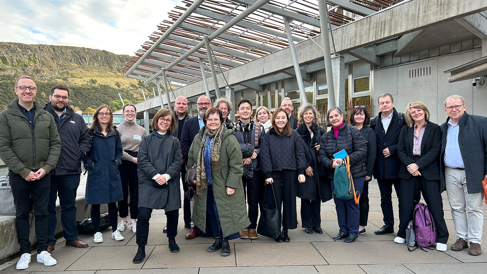A big group of people stand together outside the front entrance to The Scottish Parliament building in Edinburgh