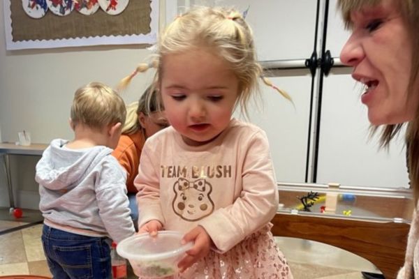 A small child plays with a 'shaker' box and her mum