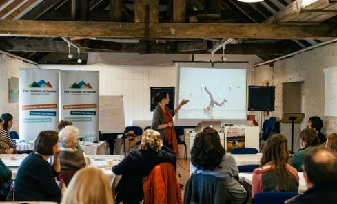 A woman stands giving a presentation in front of a small audience