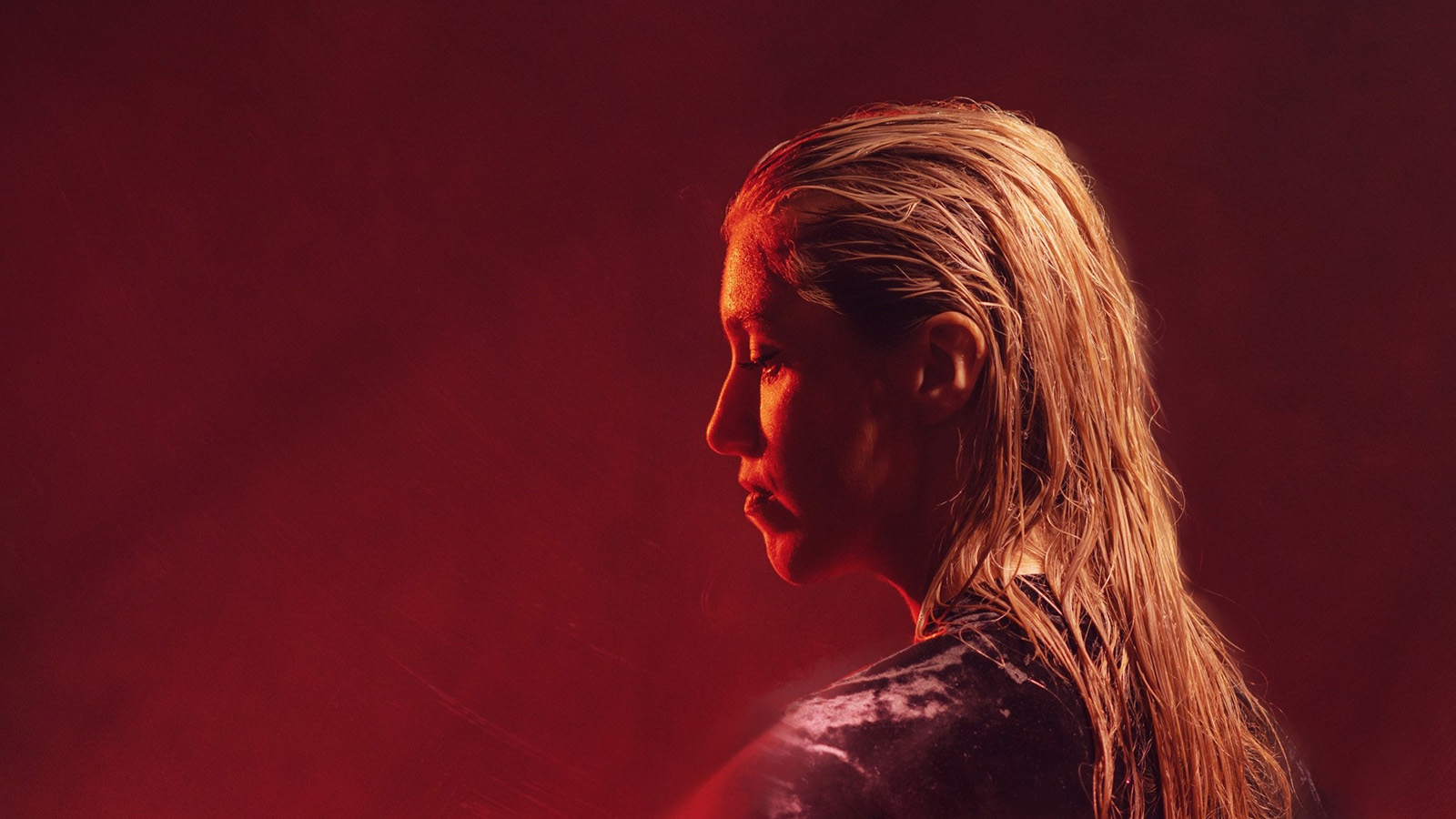 A woman (Imogen Stirling) with blonde hair caught in profile and lit in dramatic red light