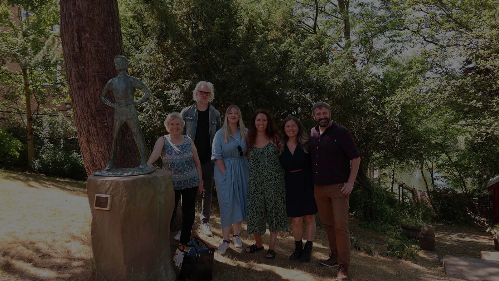 People wearing light summer clothes (these are the Bookscovery artists) pictured in a group under the shade of a leafy tree