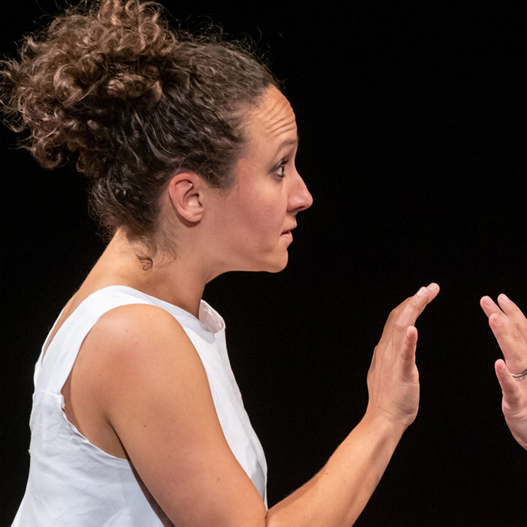 Two women in white t shirts seen in profile, looking at each other as they raise their hands palm to palm