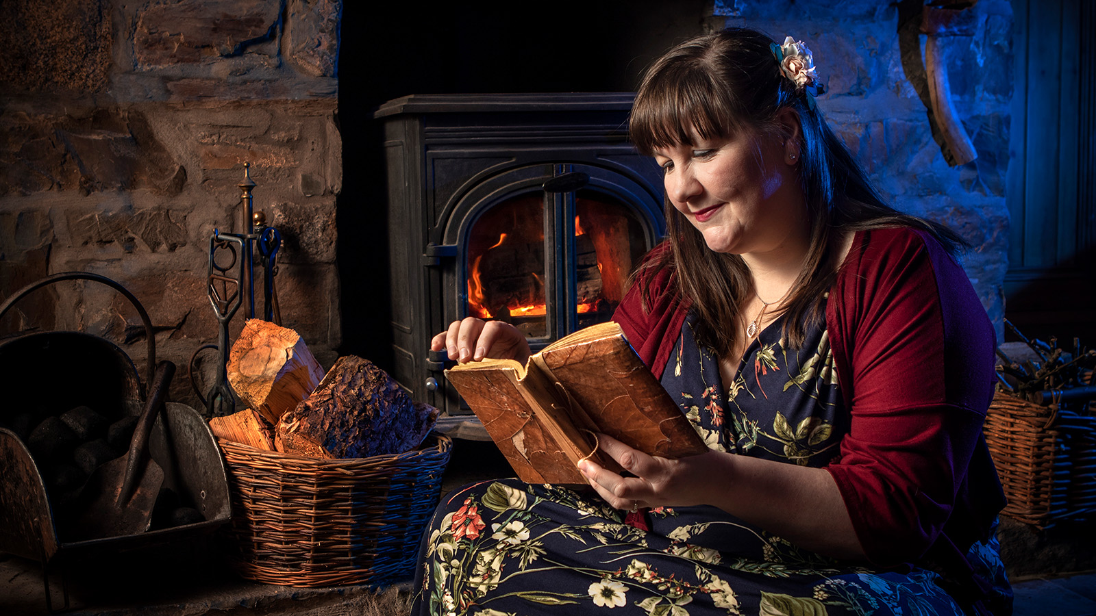 Susi Briggs looking down at a book as she sits next to a cosy fire