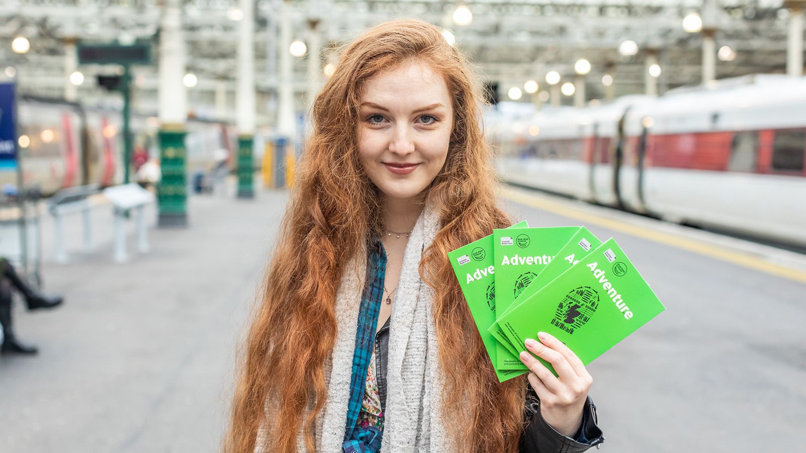 Len Pennie at Waverley train station in Edinburgh, holding up Book Week Scotland 2023 books