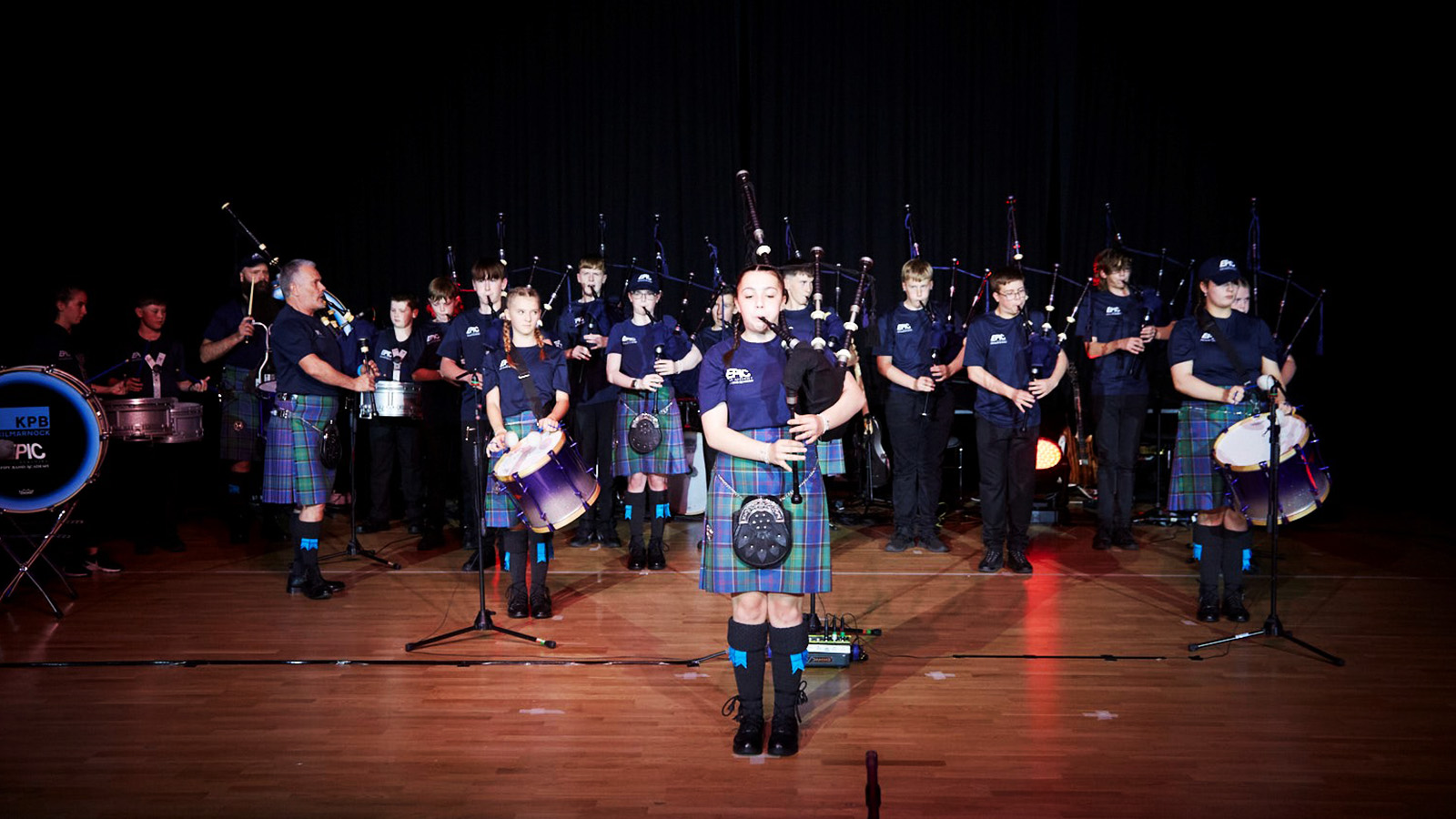 A pipe band of school pupils perform on a stage