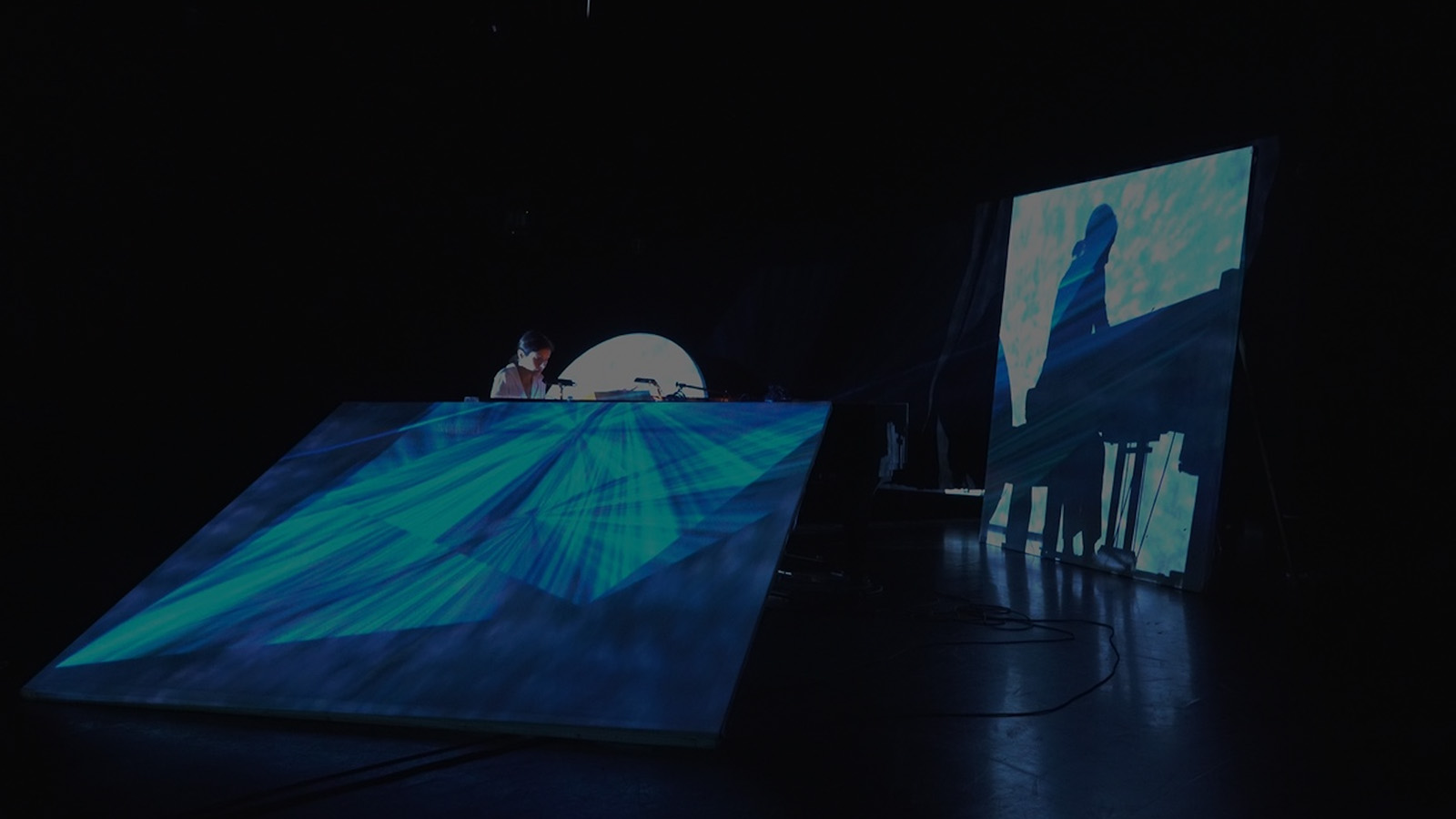 Pianist performs at grand piano on a stage lit by blue light, throwing them into shadow