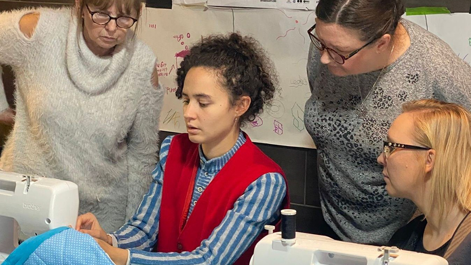 A group of women gather around a sewing machine that one of them is using