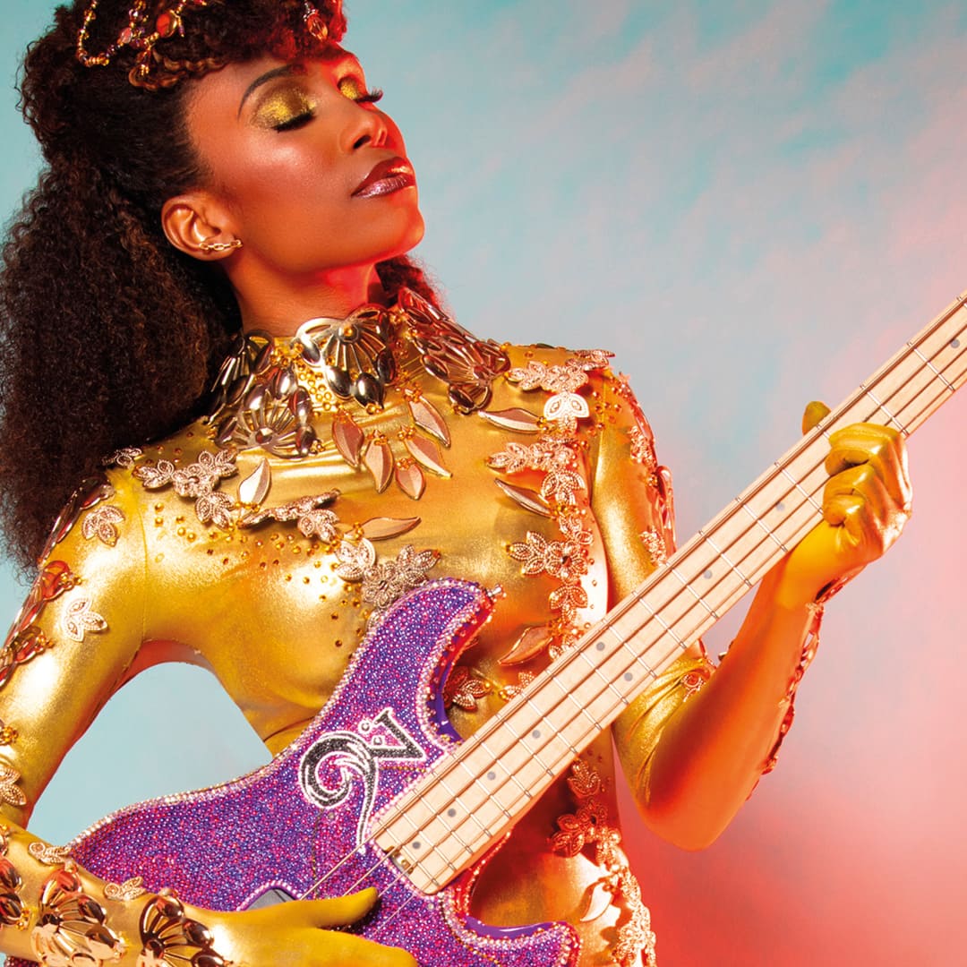 Bassist and vocalist Nik West wearing a glorious bejewelled gold headpiece and outfit playing the electric bass.