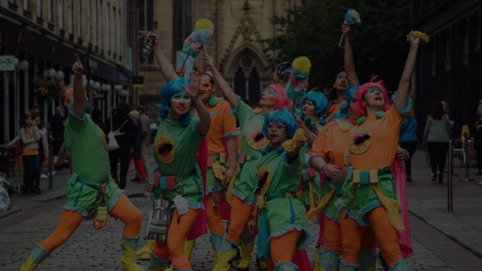 A big group of people wearing colourful superhero costumes and wigs. They're standing in a group posing and showing confidence and strength,on a city street.