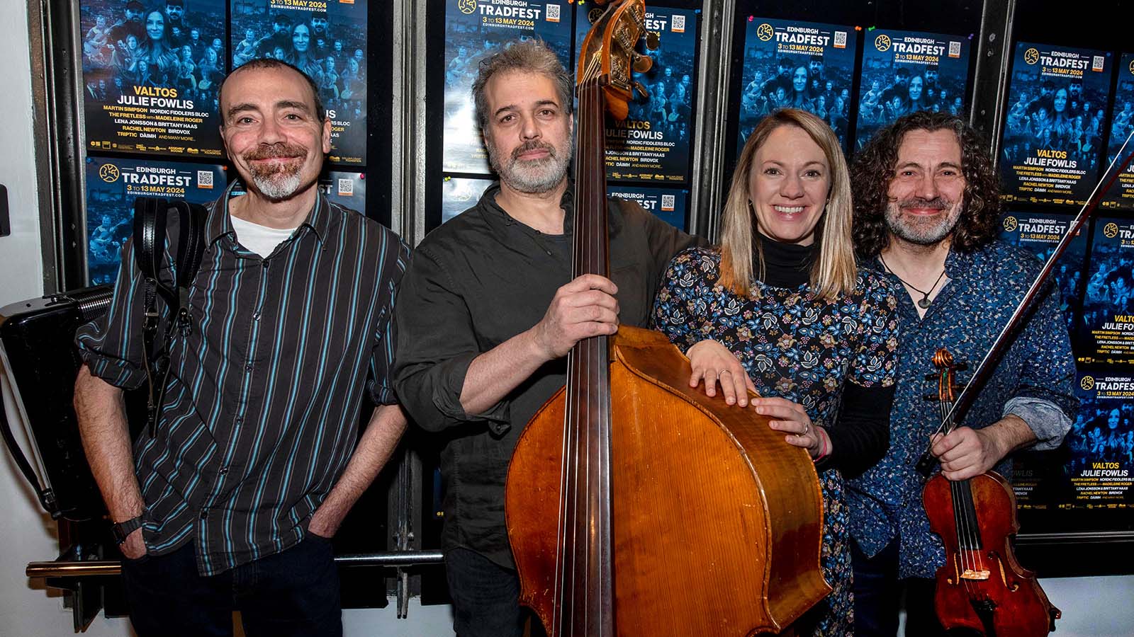 Four people - three man with instruments and a woman - pictured together in front of a wall of posters for Edinburgh tradfest