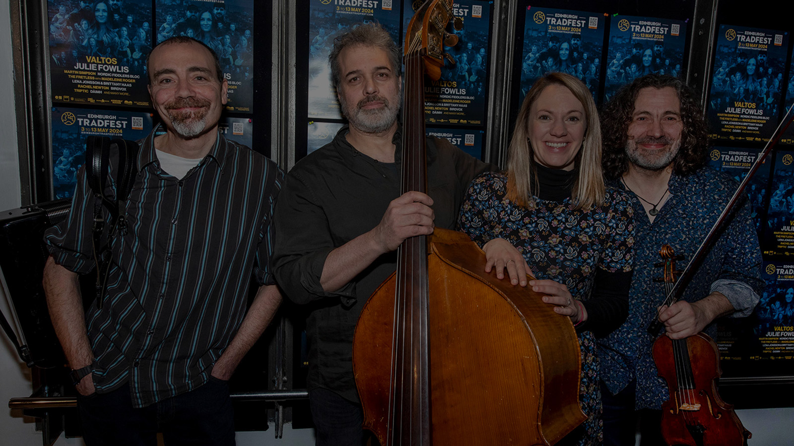 Four people - three man with instruments and a woman - pictured together in front of a wall of posters for Edinburgh tradfest