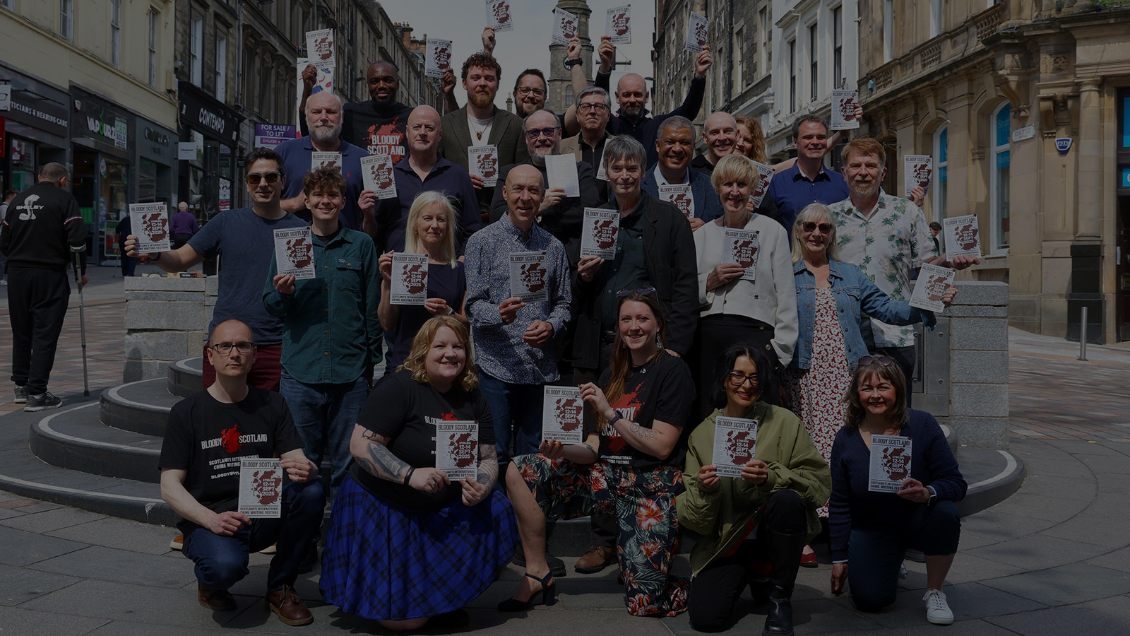 A diverse group of individuals gathers in a city square, holding event flyers for 
